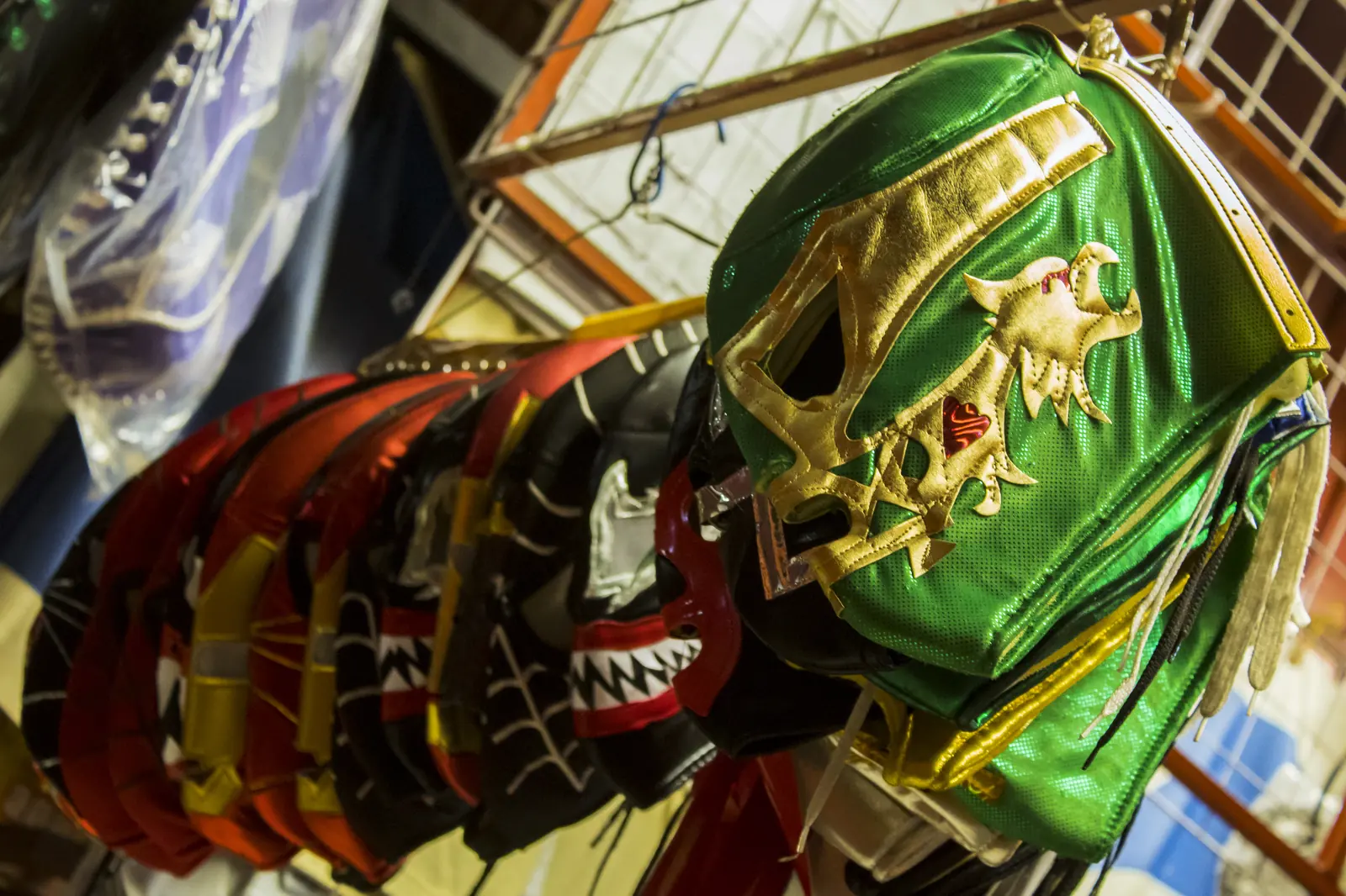 Řady masek lucha libre visí na tržním stánku, v popředí zelenozlatá maska
